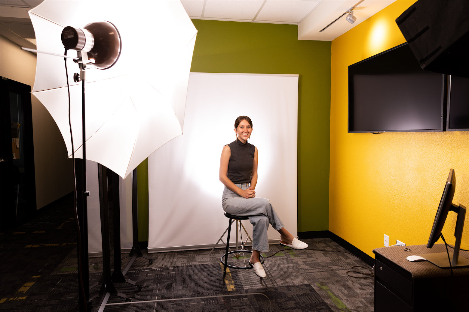 A women in front a white back drop, surrounded by professional lighting poses for a portrait.